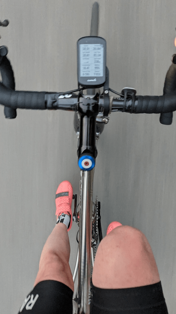 POV photo of a cyclist in motion, gliding down the road with hands off the bars and pink shoes spinning.