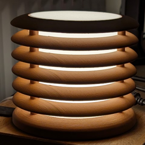 Cylindrical lamp with stacked ribbed rings and internal glow visible through horizontal gaps