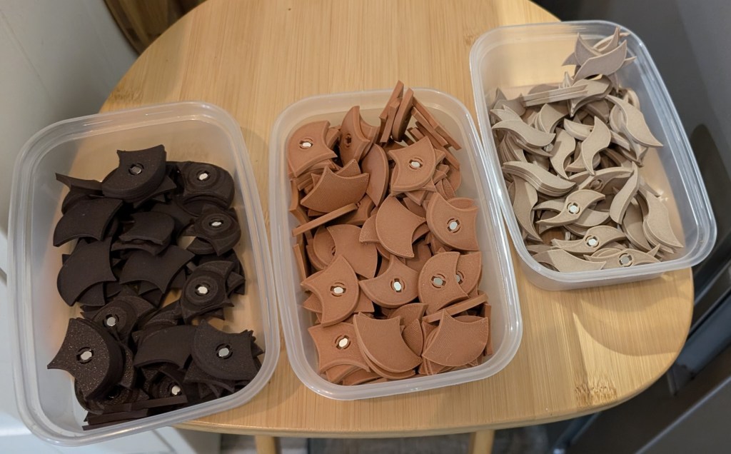 Tupperware containers filled with 3D-printed Penrose fridge magnets in dark brown, terracotta, and beige colors, neatly sorted and looking suspiciously like snacks.