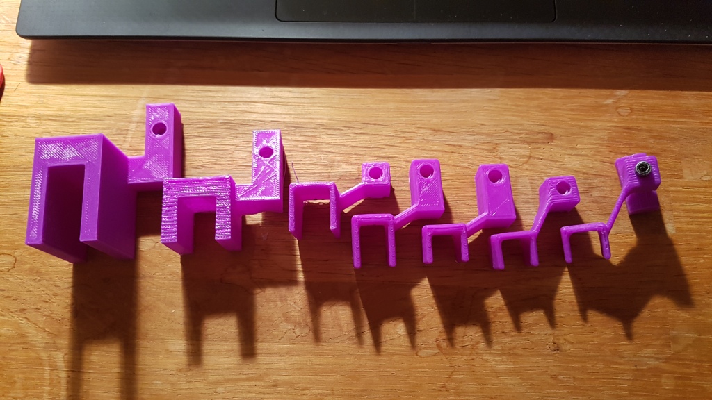 An image of a sequence of 3D prints for a chain guide. From terrible initial designs (left) that iterated to a final neat version (right).
