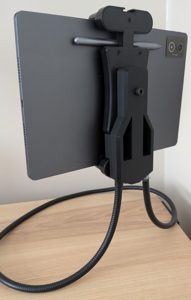 Rear close-up view of the version 2 assembly. The twin metal tips of a black gooseneck mount slot directly into the bottom of a custom 3D-printed black structural plate secured to the back of a Lenovo tablet.